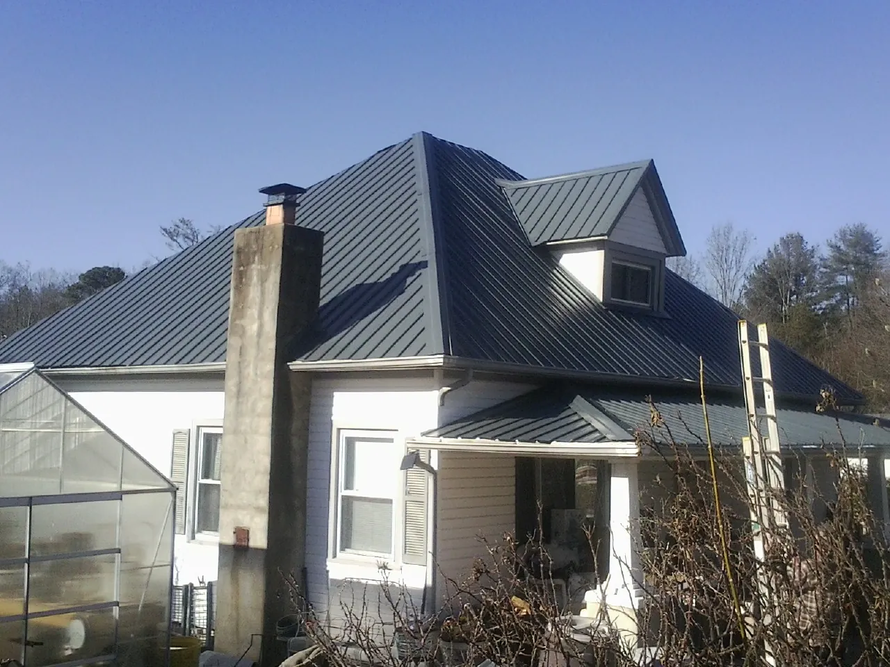 Dark blue standing seam metal roof on a white farmhouse with dormer — Slate & Tile Roof Repair by Roofing Brothers in Sandy Creek