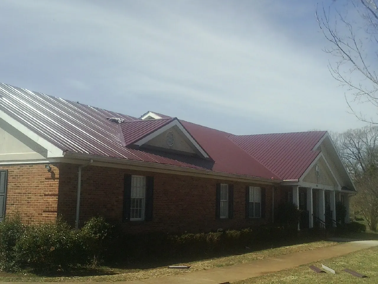 Red metal roof with gabled entries on a long brick building, from a Hail Damage Roof Repair job in Sandy Creek
