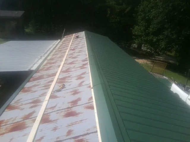 Old rusted panels beside newly installed green metal roofing — Wind Damage Roof Repair by Roofing Brothers in Sandy Creek