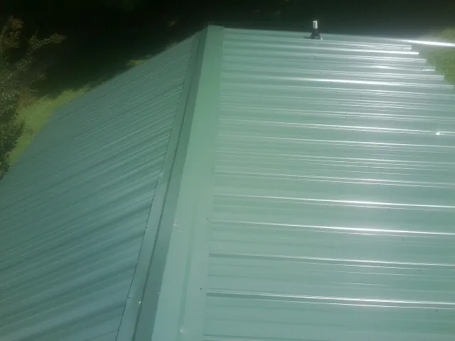New green metal panels meeting at the ridge of a roof — Flat Roof Repair work by our crew in Sandy Creek