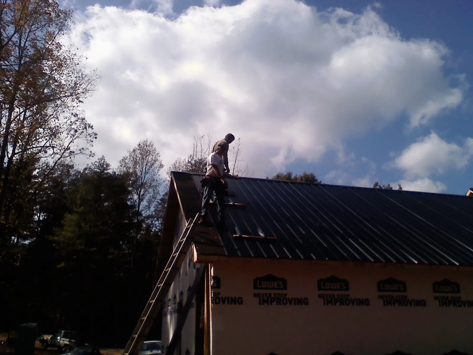 Roofer fastening dark metal panels high against a cloudy sky, from a Roof Inspection job in Sandy Creek