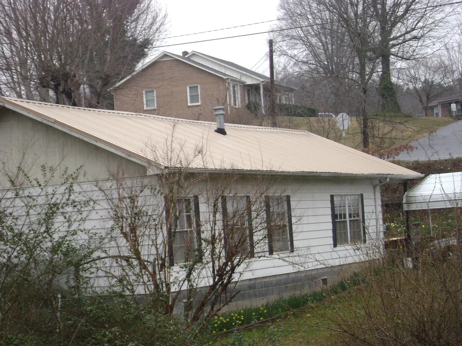 Tan metal roof on a white sided house set into a hillside — Commercial Roofing by Roofing Brothers in Sandy Creek