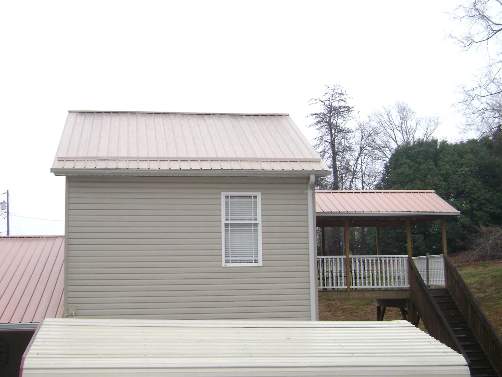 Tan metal roofs on a two story addition and attached porch, from a Roof Replacement job in Sandy Creek